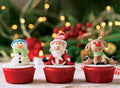 Three cupcakes with Santa Claus, snowman, and reindeer decorations against a festive background.