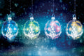 Four colorful Christmas ornaments hanging against a dark snowy background