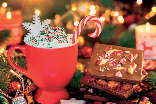 Red mug of hot chocolate with whipped cream, candy cane, and Christmas decorations on a festive background.