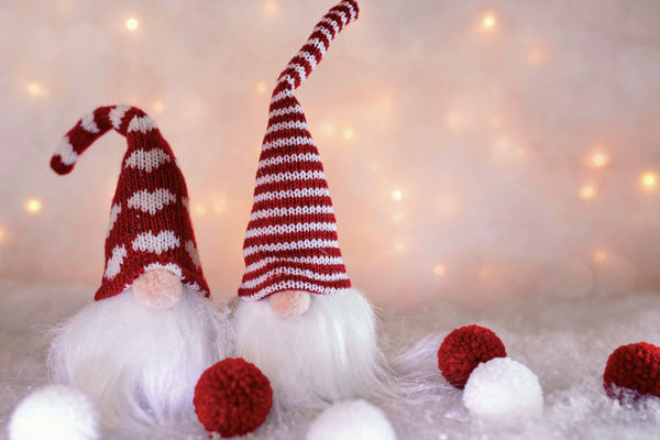 Two festive gnomes with red and white striped hats on a soft surface with blurred lights in the background.