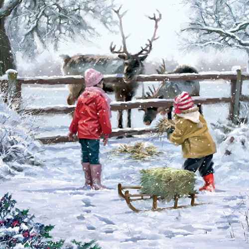 Two children in winter clothing feeding a reindeer in a snowy scene.