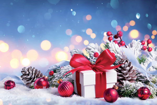 Christmas scene with a gift box, ornaments, and snowy landscape with blurred lights in the background.