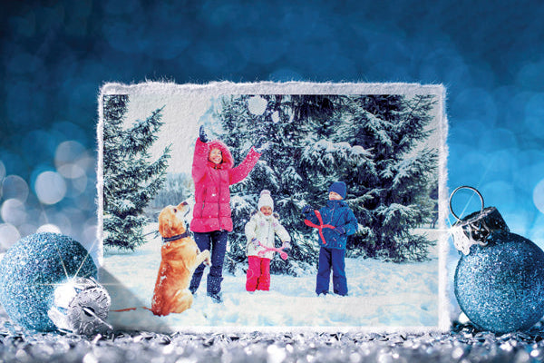 Framed photo of a family playing in the snow with a dog, surrounded by Christmas ornaments on a blue snowy background.