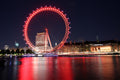 Red lit Ferris wheel at night with cityscape reflection on water