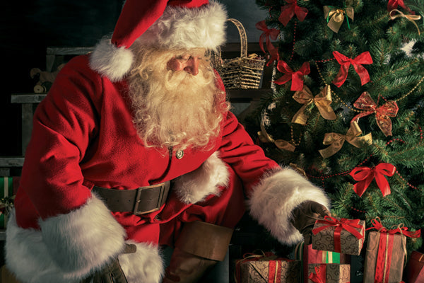 Santa Claus sitting next to a Christmas tree with presents underneath