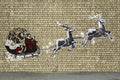 Street art of Santa Claus in a sleigh pulled by reindeer on a brick wall.