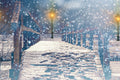 Wooden bridge covered in snow with falling snowflakes during a winter night.