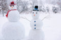 Two snowmen in a snowy landscape with trees in the background.