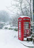 Red telephone booth covered in snow in a snowy landscape