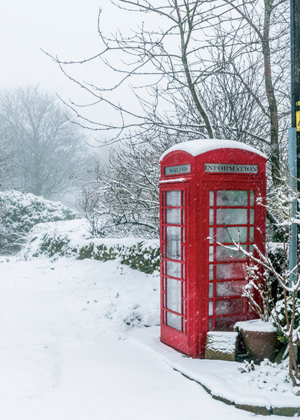 Red telephone booth covered in snow in a snowy landscape