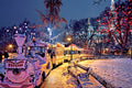 Snow-covered train in a park with festive lights and snow-laden trees at night.