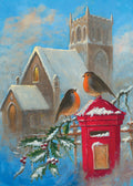 Two robins on a red postbox in front of a snowy church.