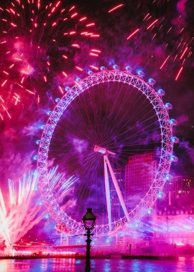 A vibrant night scene of the London Eye illuminated in pink and purple hues, surrounded by colorful fireworks exploding in the sky above the water.